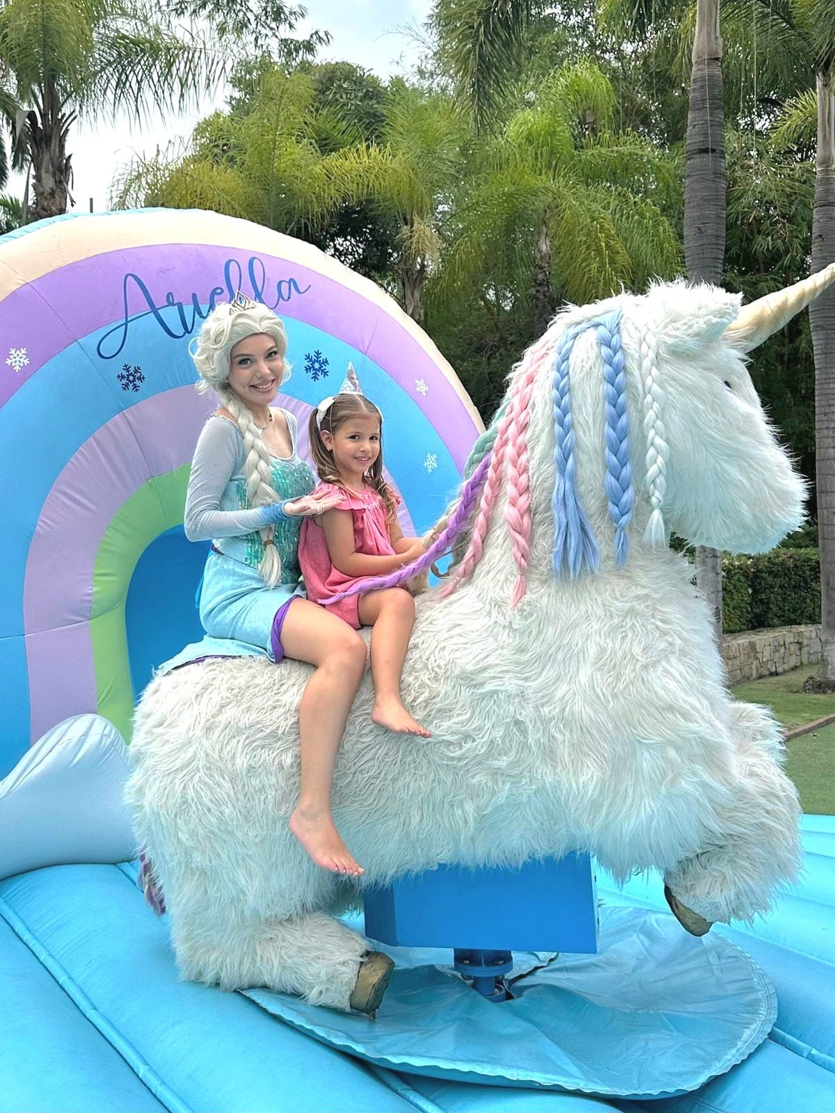 Niña con Elsa montando el unicornio inflable en fiesta temática de princesas.