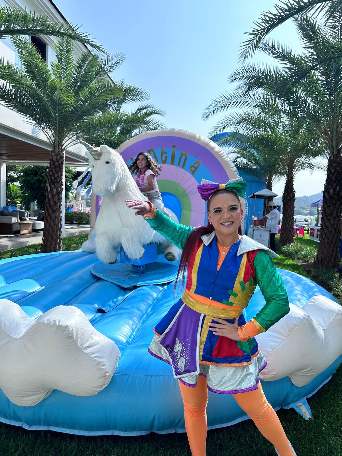 Animadora colorida junto al unicornio mecánico inflable en fiesta de cumpleaños.